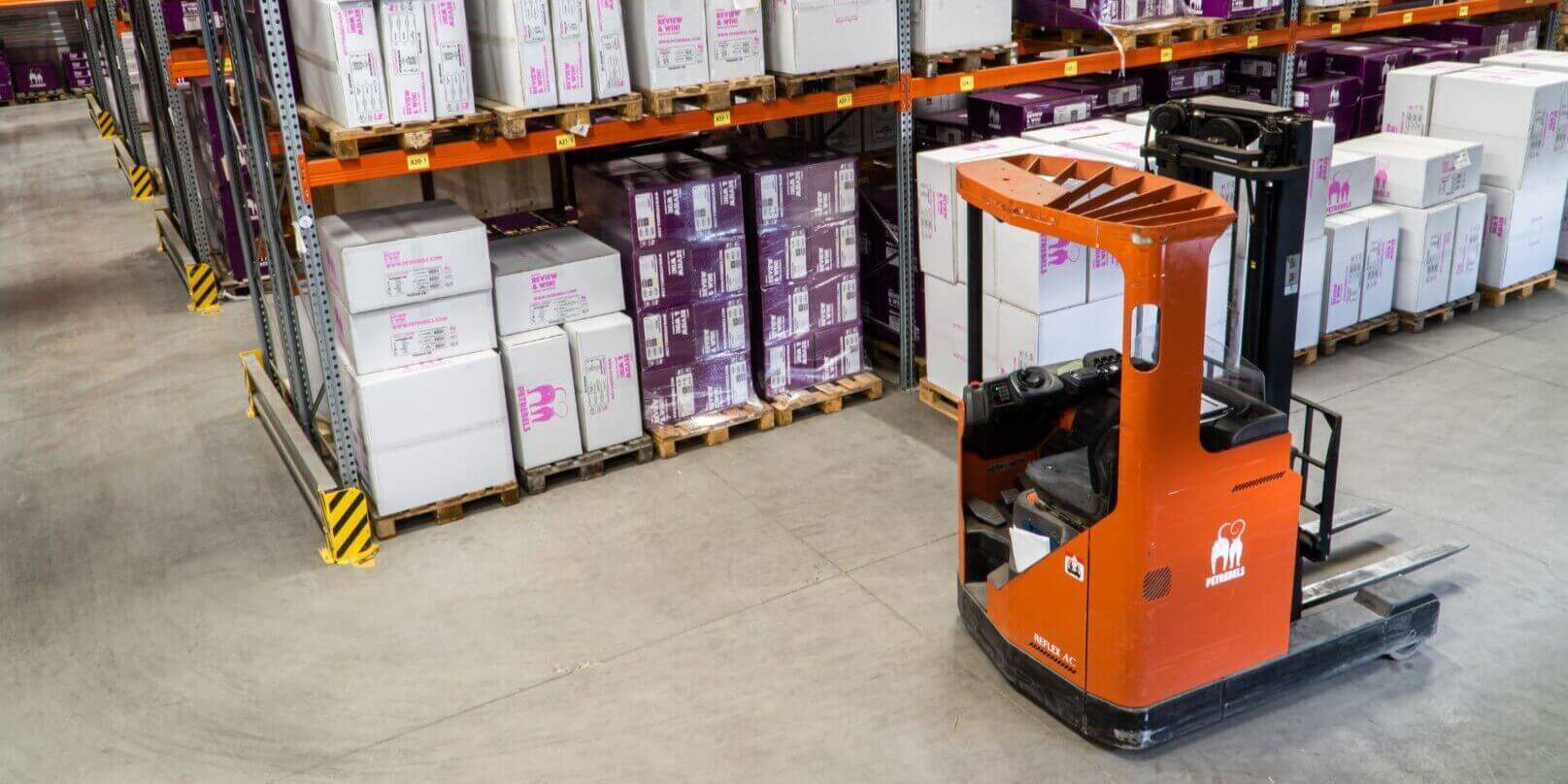 Carretilla elevadora en almacén industrial organizado con estanterías llenas de cajas.