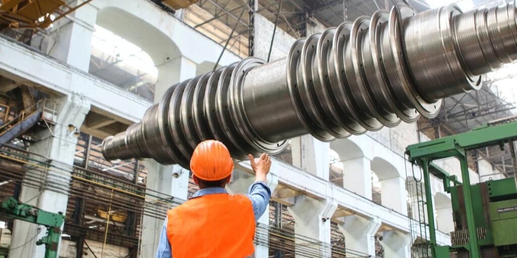 Operario guiando componente metálico en planta de calderería industrial