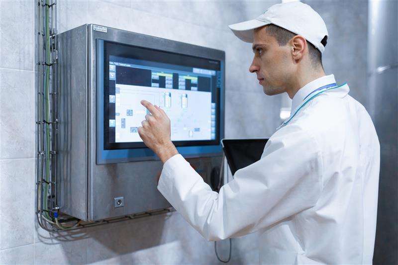 Técnico operando pantalla táctil de sistema MES en planta industrial automatizada.