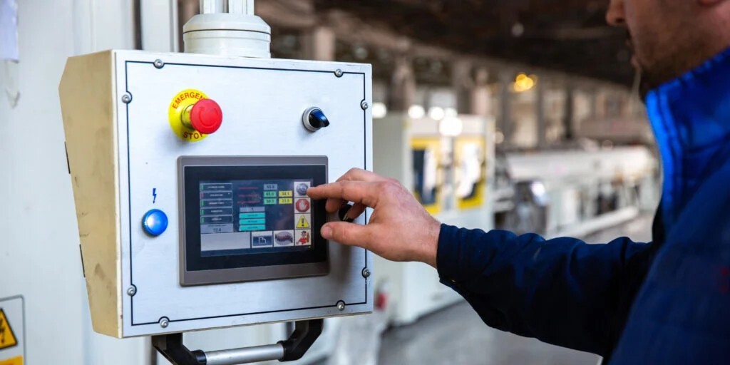 Operario utilizando pantalla táctil de control industrial en planta de producción.